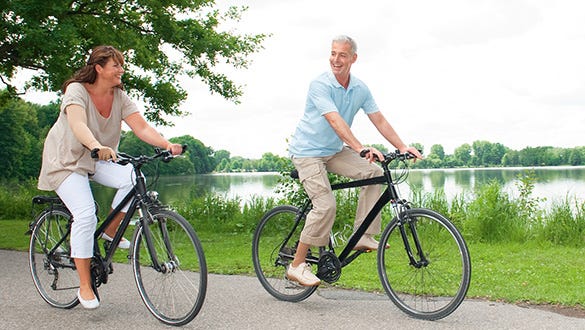 elderly couple being active on their holiday by biking alongside a lake