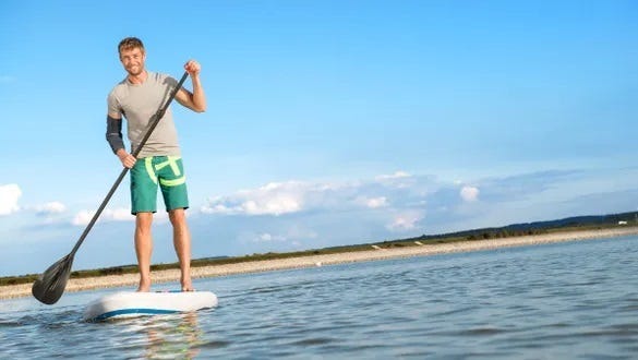 Man floating  on his stand up paddle through a lake showcasing his medi elbow brace