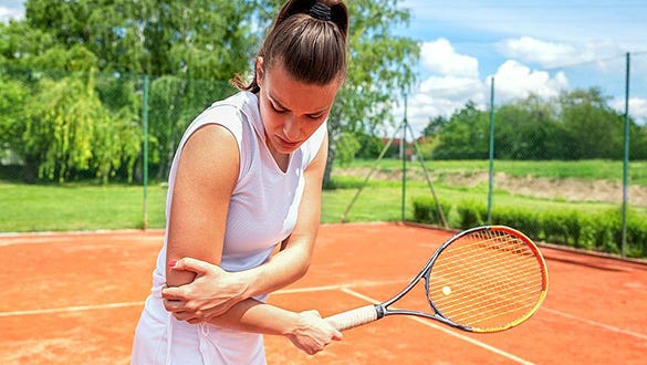 Woman stadning  in her tennis gear on a tennis court stabilising her hurtful elbow