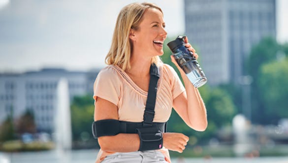 Female showcasing a medi arm sling and drinking water out f a bottle