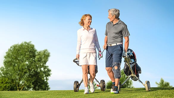 elderly couple with golfbags strolling across a golfcourt while the man is wearing a medi knee brace