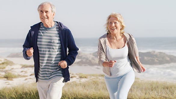 elderly couple jogging along the dunes at the sandy beach of their holiday destination