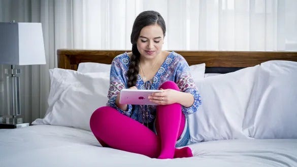 Female on bed using tablet, showcasing compression  stockings for Lymphoedema management