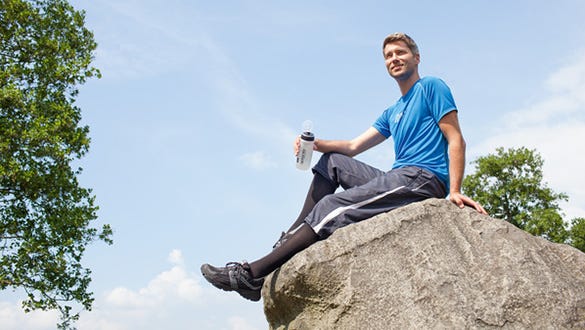 men sitting on a rock enjoying his drink after a sunny hike on his active holiday