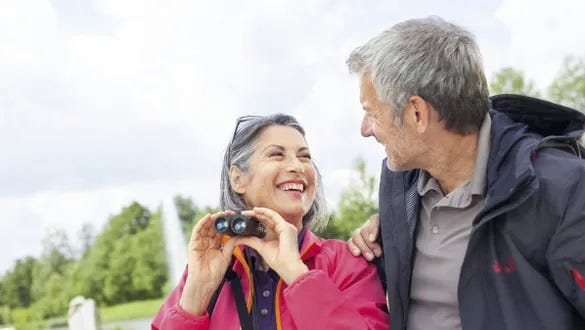 Elderly coupling smiling at each other after seeing something exciting with their binocular