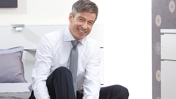 White-collar worker  sitting comfortable on his bed smiling while waiting for his travels to start