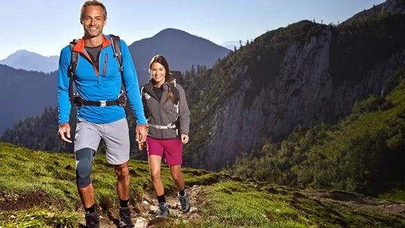 couple hiking on a rocky trail up the sunny mountains, men wearing medi knee support 