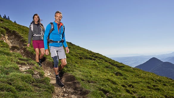 couple hiking on a rocky  trail down the sunny mountains, men wearing medi knee support 