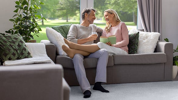 Woman wearing compression stockings sitting happily next to her husband on her couch 