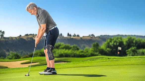 Elderly man wearing a medi knee brace playing golf on a golf court 