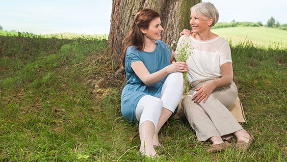 Two woman sitting under a tree chatting with each other happily and admiring their flowers
