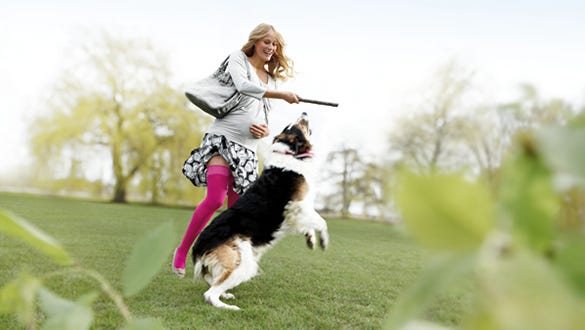 "pregnant woman playing with her dog while  showcasing her pink medi compression stockings