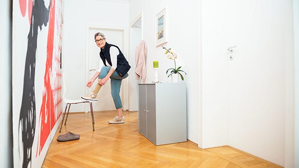 A woman suffering from venous leg ulcer standing in her wardrobe, tying her shoes to head out.